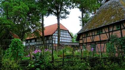 Fachwerkhäuser mit Reet- und Ziegeldach im Freilichtmuseum Diesdorf, umgeben von Bauerngarten und Holzzaun